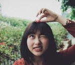 A young woman playfully holds a flower outdoors, expressing joy and charm.